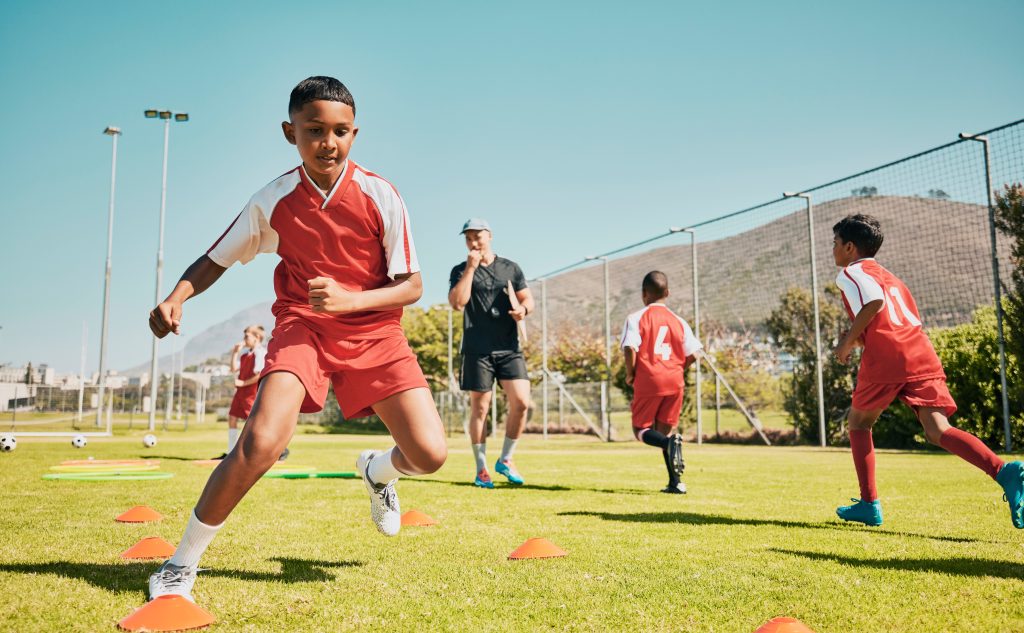 Children completing soccer drills with a coach on a grass field
